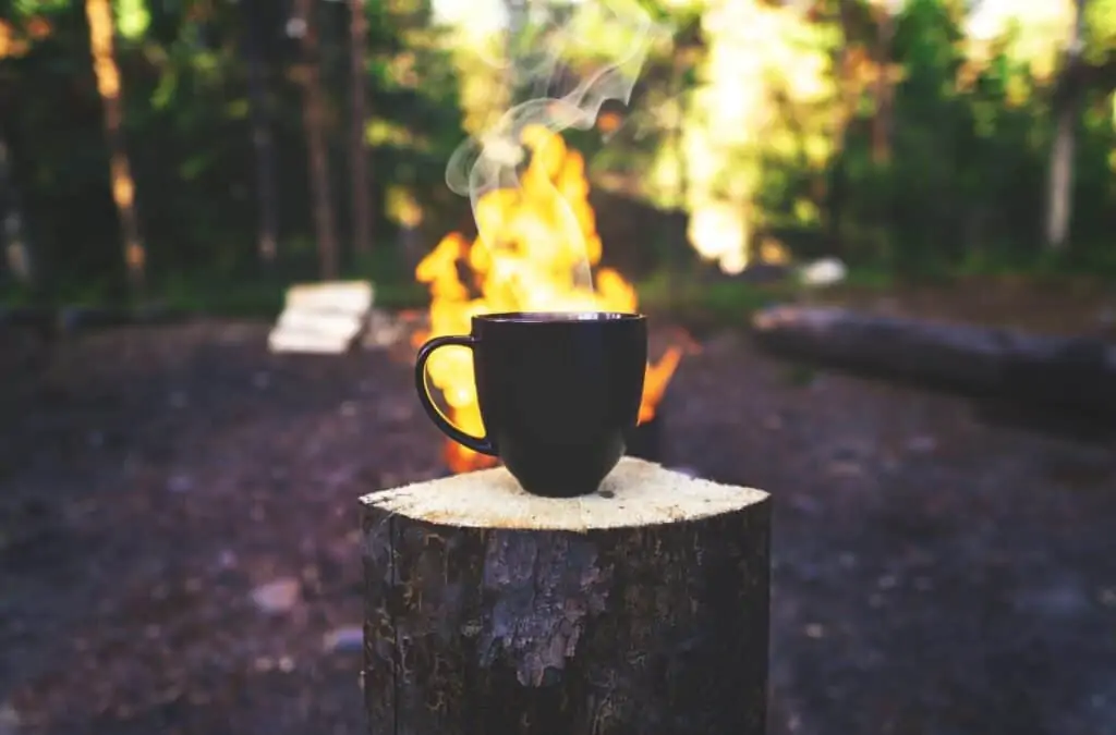 Eine Tasse Kaffee vor einem Lagerfeuer